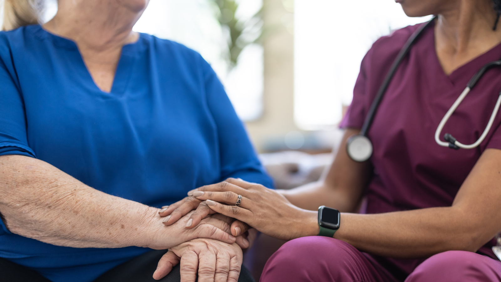 Close up image of patient feedback: a patient in a blue top is comforted by a doctor in a purple outfit.